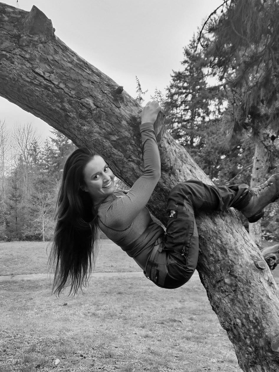 This is a black and white photo of our tree care specialist Meg! She is hanging off of a tree trunk.